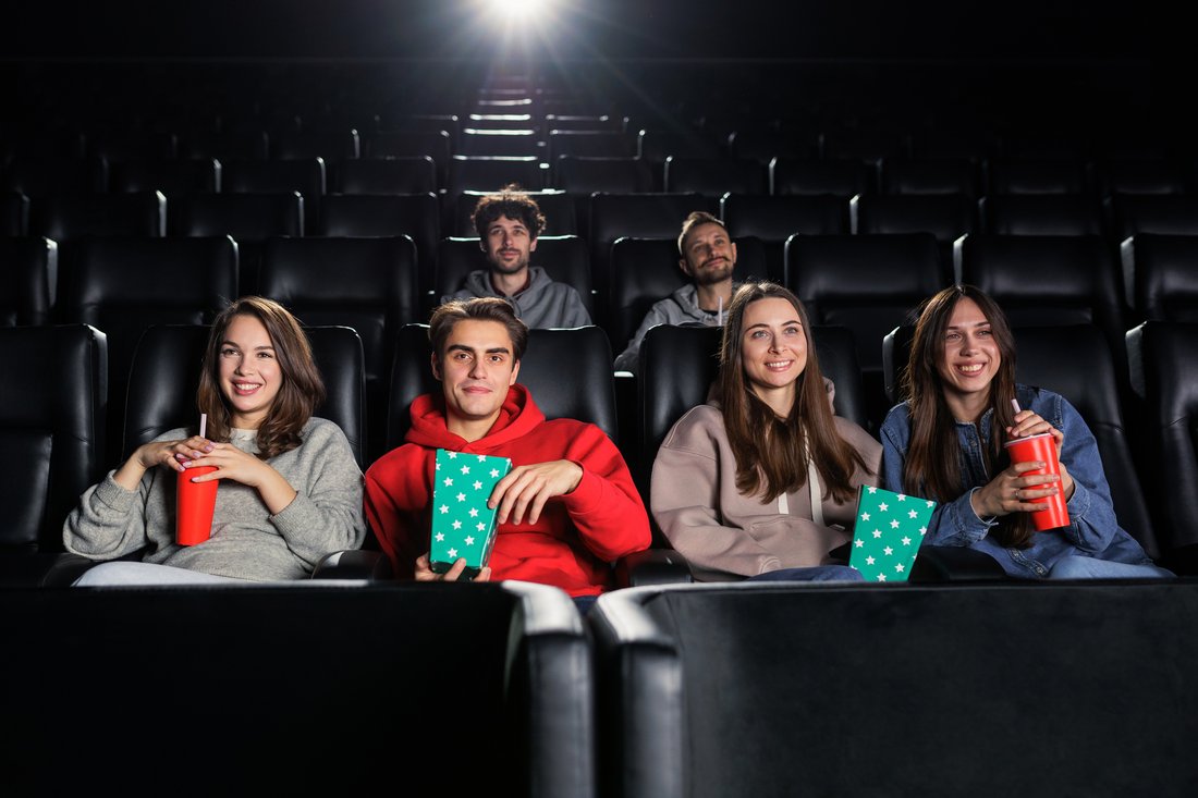 Znajomi z popcornem siedzą w fotelach kinowych